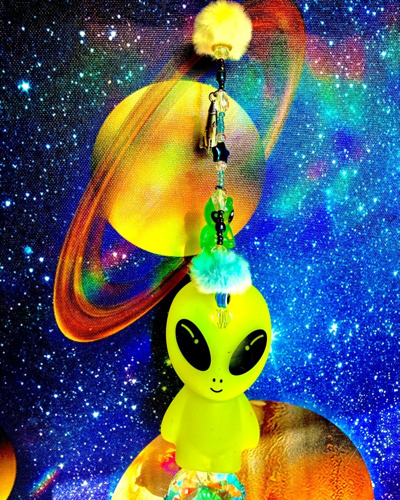 Beaded sun catcher with a green alien, a ringed planet charm and a yellow pom-pom.