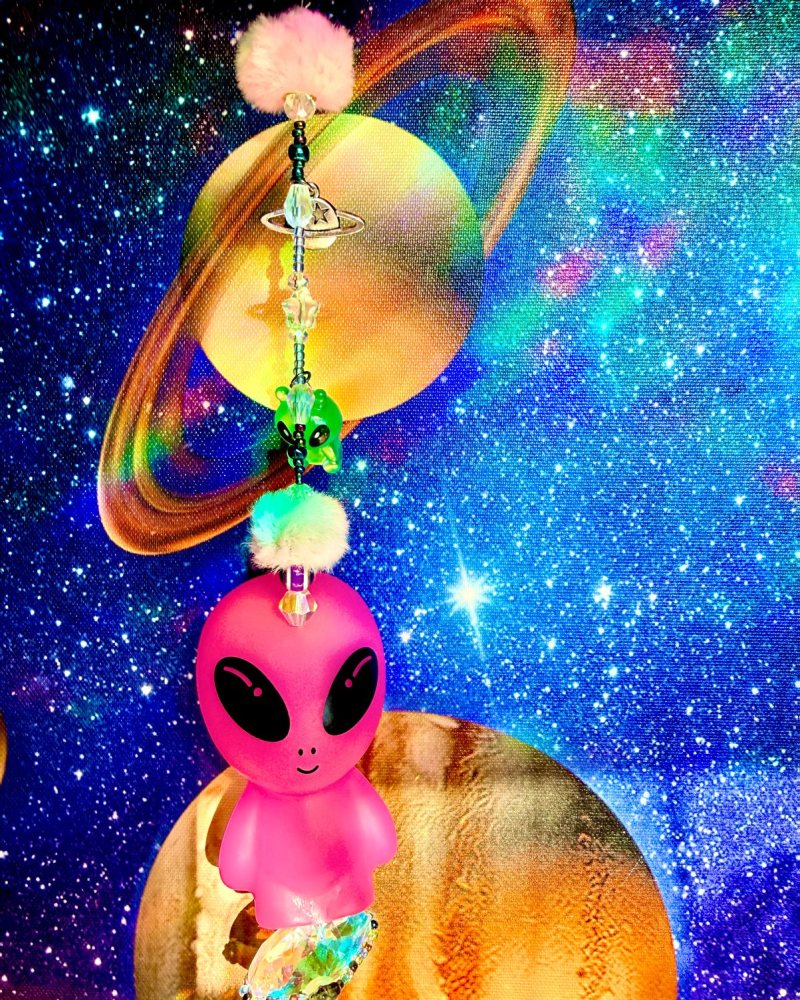 Beaded sun catcher with a pink alien, a ringed planet charm and a pink pom-pom.