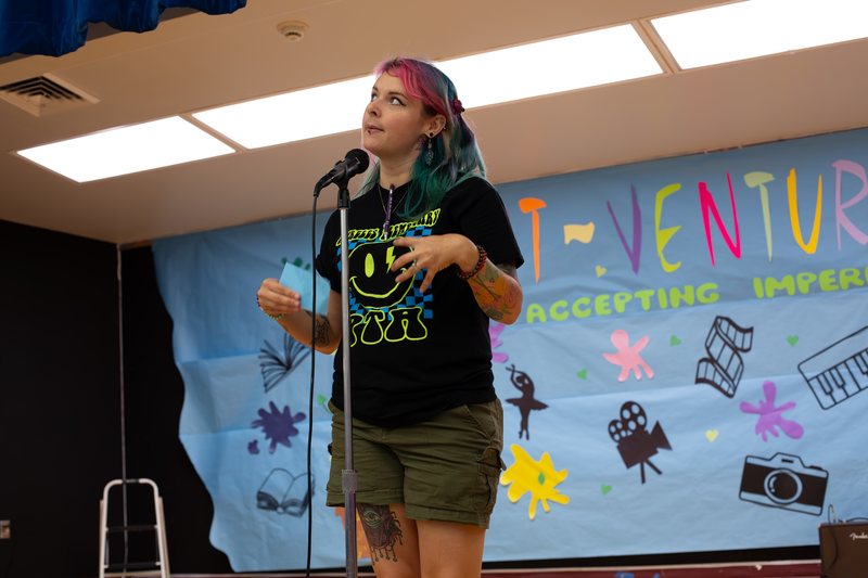 Shai at a microphone in front of an ArtVenture banner that says accepting imperfection